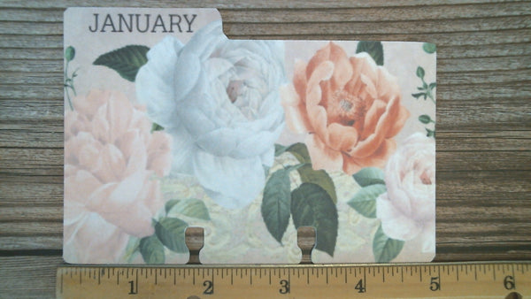 A January 3 x 5 Rolodex divider. It is decorated with cabbage roses in shades of pink and coral with green leaves. Underneath the divider is a ruler, showing the width to be 5 inches.