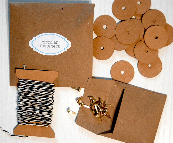 An envelope that says "circular fasteners", 21 brown circles with holes in the center, 21 gold brads in an envelope, and 130 inches of twine on a cardstock spool. This is part of the 10 envelope kit.