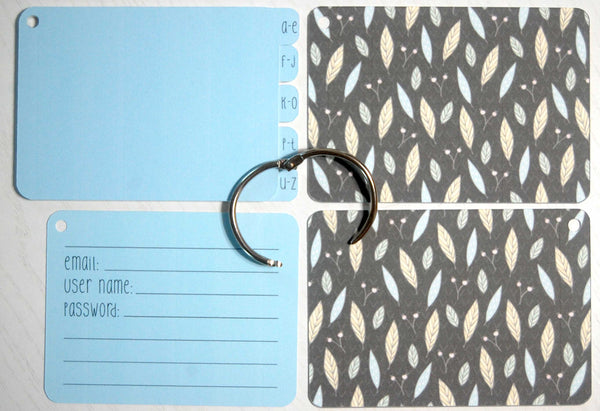 Flat lay display of all of the elements of the Falling Leaves password keeper: Front and back cover, silver ring, 5 blue dividers, and 40 blue password cards
