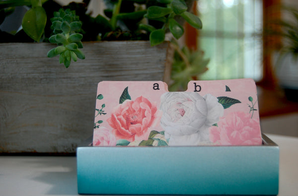 Pink and white roses on a Rolodex Divider in  pretty holder with plants in the background