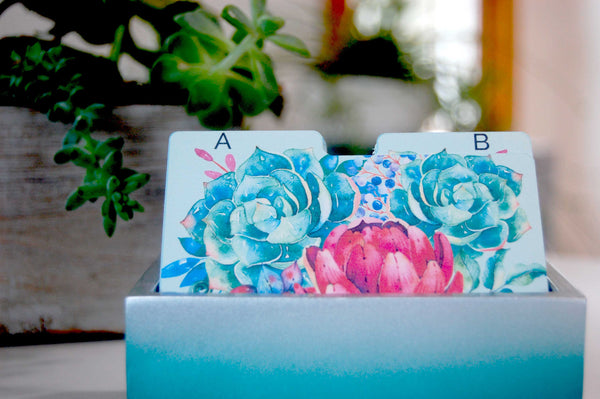 Mint green Rolodex Dividers with a green, blue, and pink succulent print in a pretty holder with plants in the background