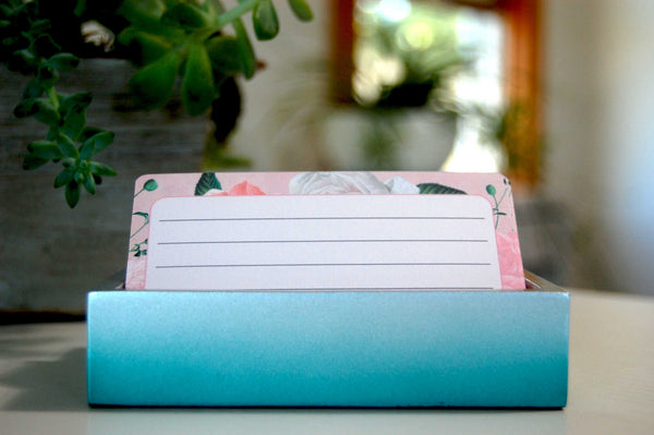 Colorful floral vintage rose Rolodex refill cards in pink and white and green. The cards are ruled and in a teal holder.  There are plants in the background.