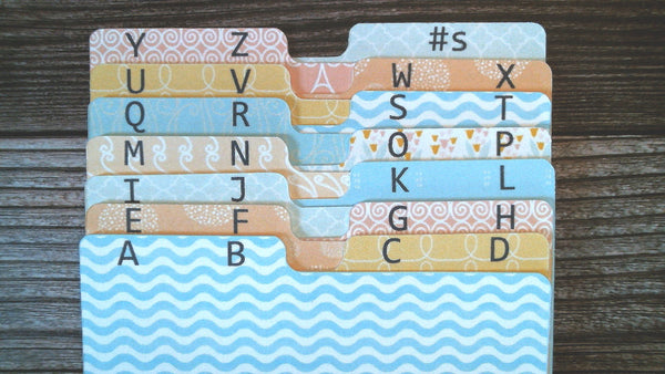 Pastel Rolodex dividers in 9 different patterns. There are 2 letters per divider. The first divider has A B in black on the tab. The divider is a wavy pattern in alternating stripes of sky blue and white.