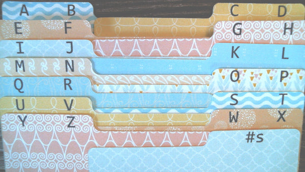 A close-up of decorative alphabet file Rolodex tabs arranged in rows, featuring pastel patterns with black uppercase letters from A to Z in black.