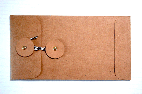 Handmade Kraft Envelope with Twine Closure: This brown rectangular envelope was made from a kit. It has two brown circular tabs attached with gold brads. A piece of black and white twine is wrapped around the circles to close the envelope.