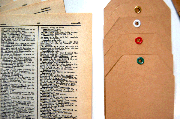 Close up of yellowed vintage-looking dictionary pages and kraft cardstock tags with metal eyelets in different colors.