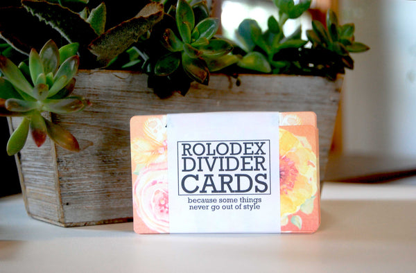 Floral Watercolor Rolodex Dividers: They are wrapped in a bundle of 13. The wrapper is white with black letters and says "ROLODEX DIVIDER CARDS: because some things never go out of style." There is a succulent plant in the background.