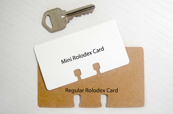 A white tiny Rolodex card next to a key and a brown Regular sized Rolodex card for size comparison