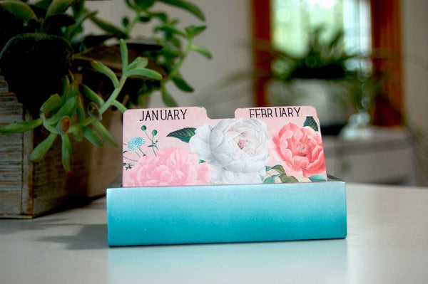 Pretty Floral Monthly Rolodex Dividers in a vintage shabby rose print. The January and February tabs are visible. They are in a Rolodex holder with plants in the background.